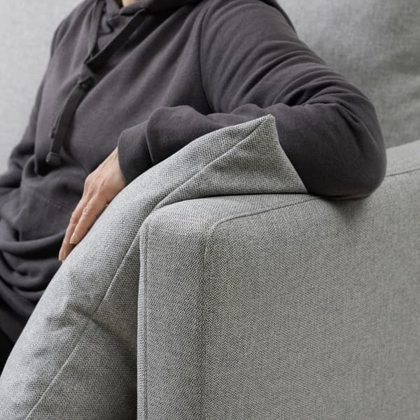 Una persona sentada en un sofa apoyado en brazo en la reposera con un cojín del mismo color gris.