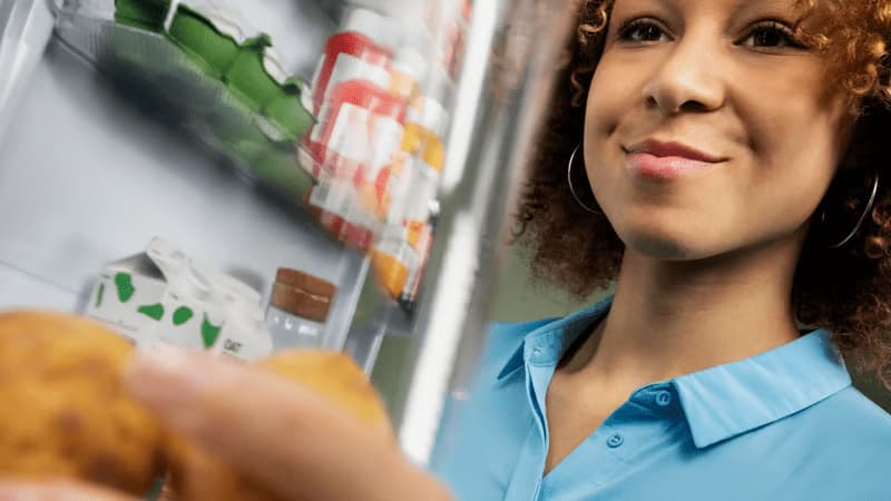 Una persona sonriente se acerca a un frigorífico para coger algo.