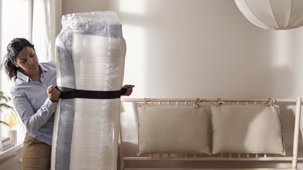 Una persona sta chiudendo un materasso arrotolato accanto ad un  letto matrimoniale