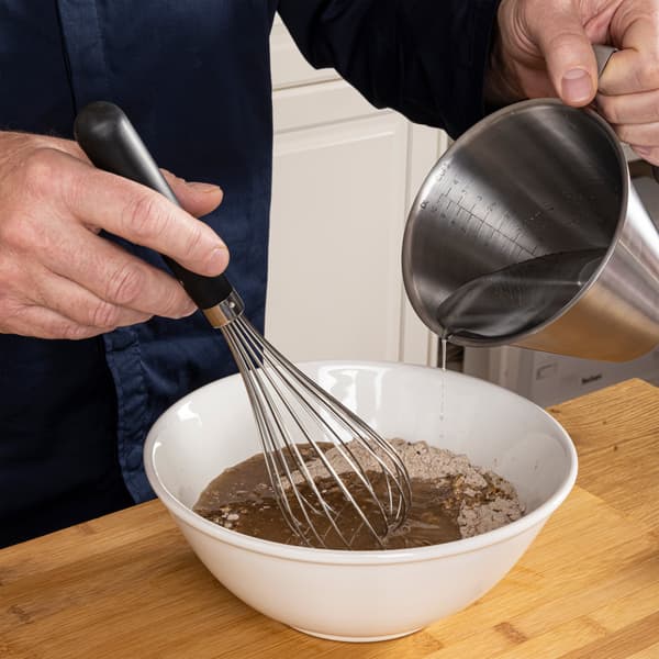 Una persona versa acqua in una ciotola capiente con il preparato per pane ai multicereali KNÅDA all'interno.
