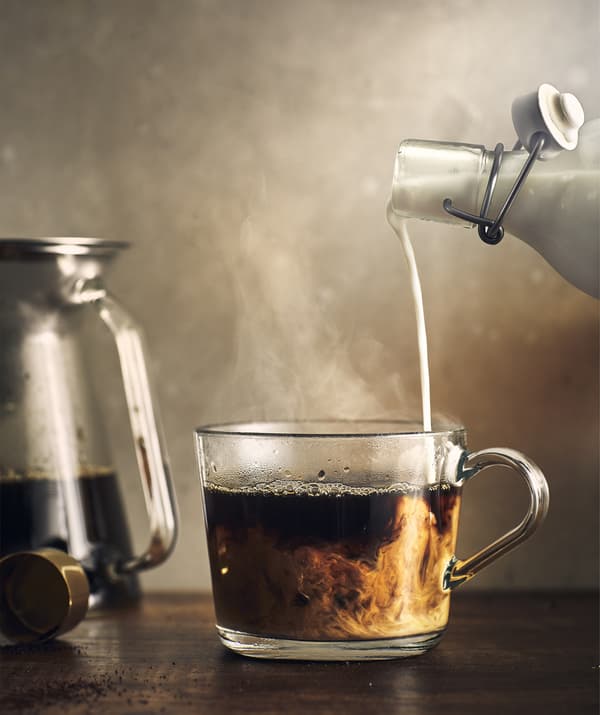 Una persona versa del latte in una tazza da caffè in vetro - IKEA