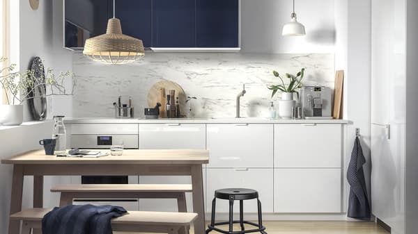 Una piccola cucina con cassetti bianchi e frontali lucidi nero-blu, più un tavolo in legno con due panche.