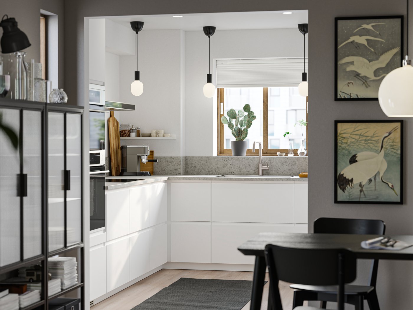 Una piccola cucina con frontali VOXTORP bianco opaco lisci, tre lampade a sospensione nere e una zona pranzo in primo piano - IKEA