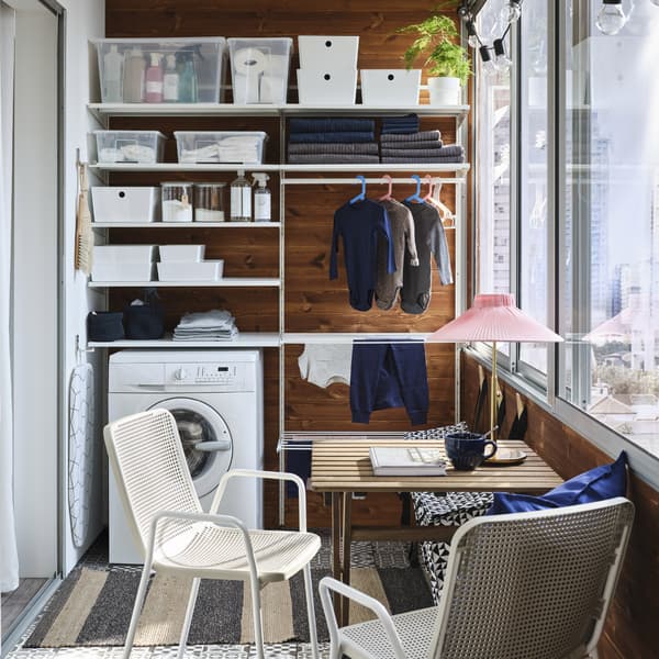 Una piccola veranda con una parete attrezzata a lavanderia bianca, una lavatrice, un tavolo da giardino e due sedie bianche/beige - IKEA