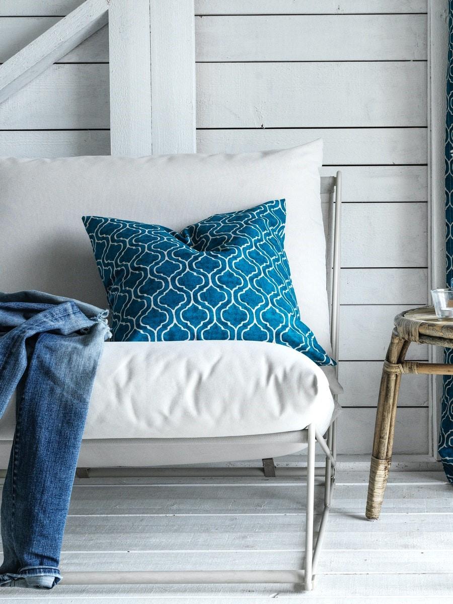 Una poltrona bianca con un cuscino a trama geometrica e accanto un paio di jeans. A lato, tavolino.