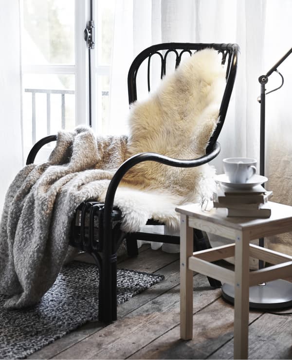 Una poltrona con una pelle di pecora LUDDE e un plaid. Accanto uno sgabello ODDVAR con libri, una tazzina con piattino e un paio di occhiali.