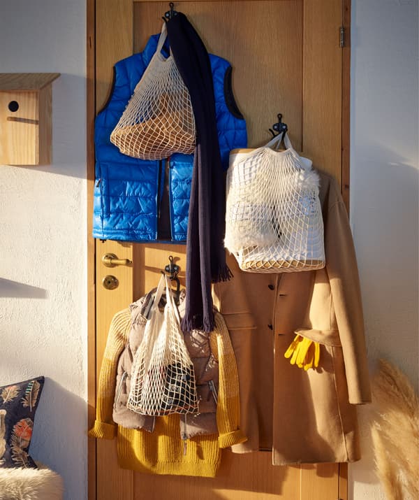 Una porta in legno con appesi i cappotti degli ospiti e alcune borse a rete contenenti i loro oggetti personali - IKEA