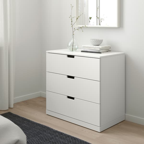 Una recámara luminosa de estilo escandinavo con una cómoda NORDLI blanca IKEA con algunos libros y un florero encima.