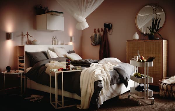 Una rete annodata sopra un letto con lenzuola morbide, cuscini e coperte, un carrello carico di snack e bevande - IKEA