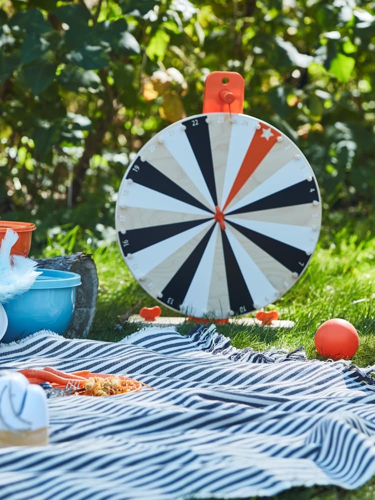 Una ruota in un giardino con un telo a righe sull'erba. Sopra, un piatto con del cibo e dietro delle ciotole chiuse con coperchio GARNITYREN.