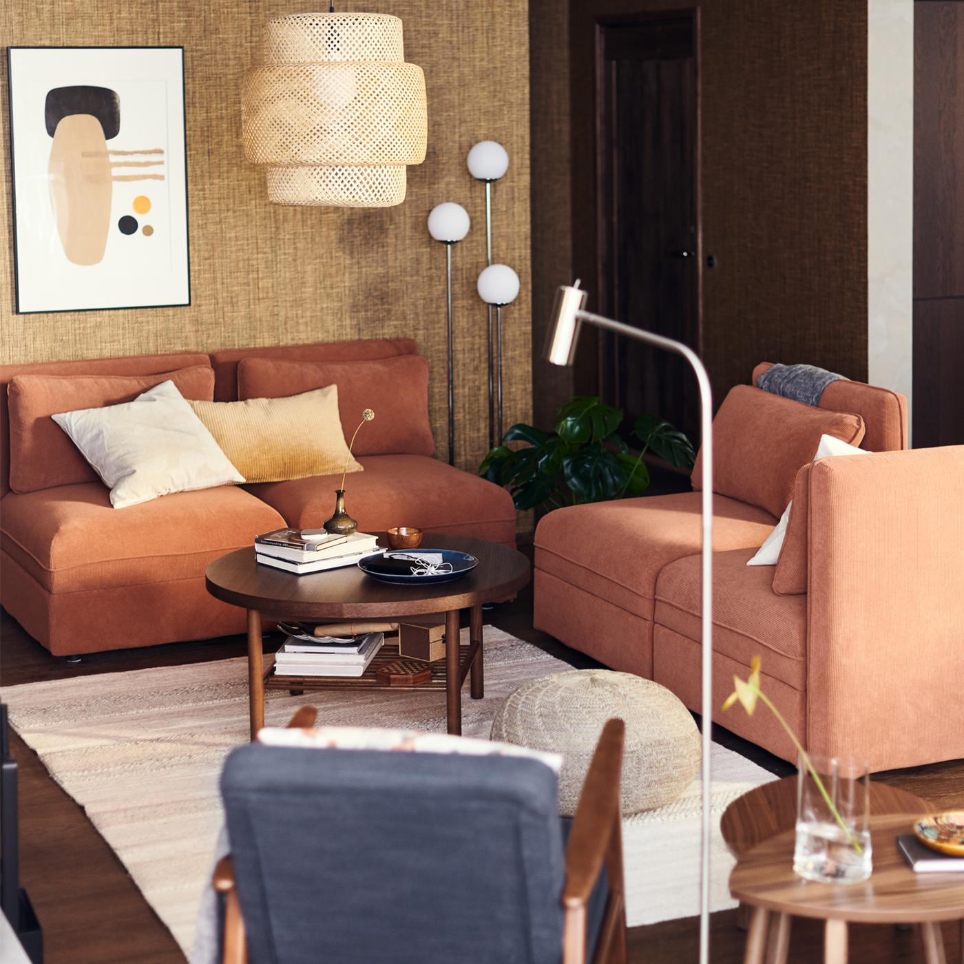 Una sala con sofás modulares VALLENTUNA en color óxido bajo una lámpara de techo SINNERLIG de bambú.