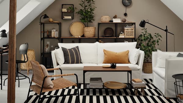Una sala con un sofá blanco de tres plazas y un sillón ancho de una plaza, un tapete plano y muebles de la serie FJÄLLBO.