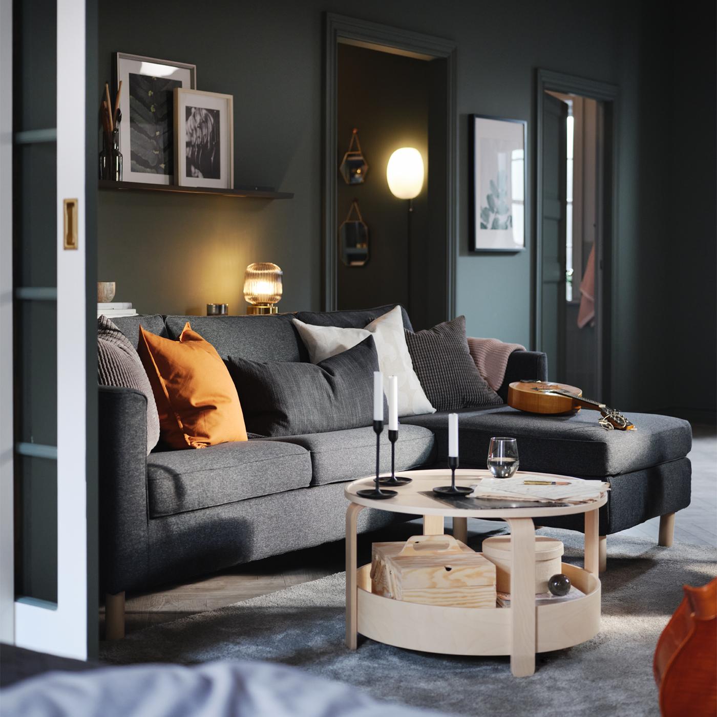Una sala con una mesa de centro BORGEBY de chapa de abedul frente a un sofá de 3 asientos PÄRUP de color gris oscuro con chaise longue.