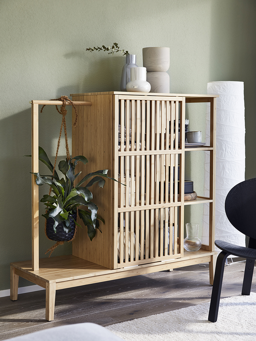 Una scaffalatura in legno con ante a doghe, piante in vaso e vasi decorativi, su uno sfondo di parete verde chiaro e una sedia nera.