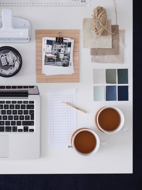 Una scrivania ben organizzata con due tazzer di thè, computer, fogli, foto su blocchetto e contenitore con graffette. 