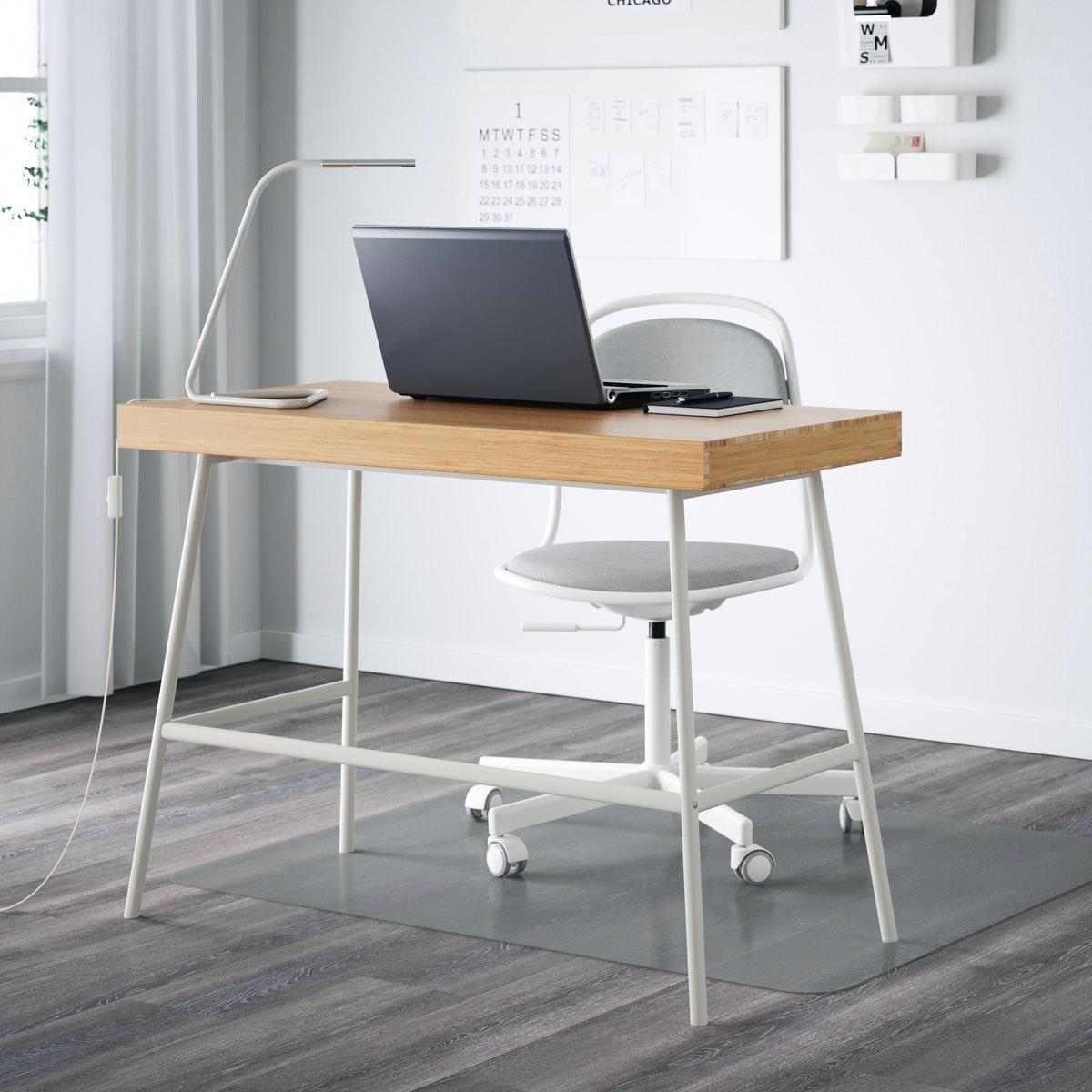Una scrivania bianca LILLÅSEN e in legno con una sedia girevole ÖRFJÄLL e una protezione per pavimento KOLON. Sopra, un laptop aperto e una lampada a LED HÅRTE da lavoro.