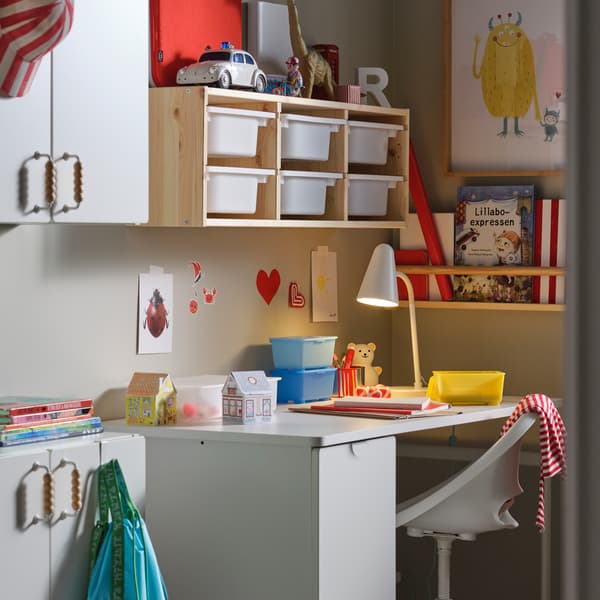 Una scrivania con elemento estraibile LÄRANDE bianca, una sedia da scrivania per bambini bianca e una combinazione di pensili in pino/bianco SMÅSTAD. Sopra la scrivania c'è una combinazioni di contenitori TROFAST e accanto un elementp da parete FLISAT con dei libri.