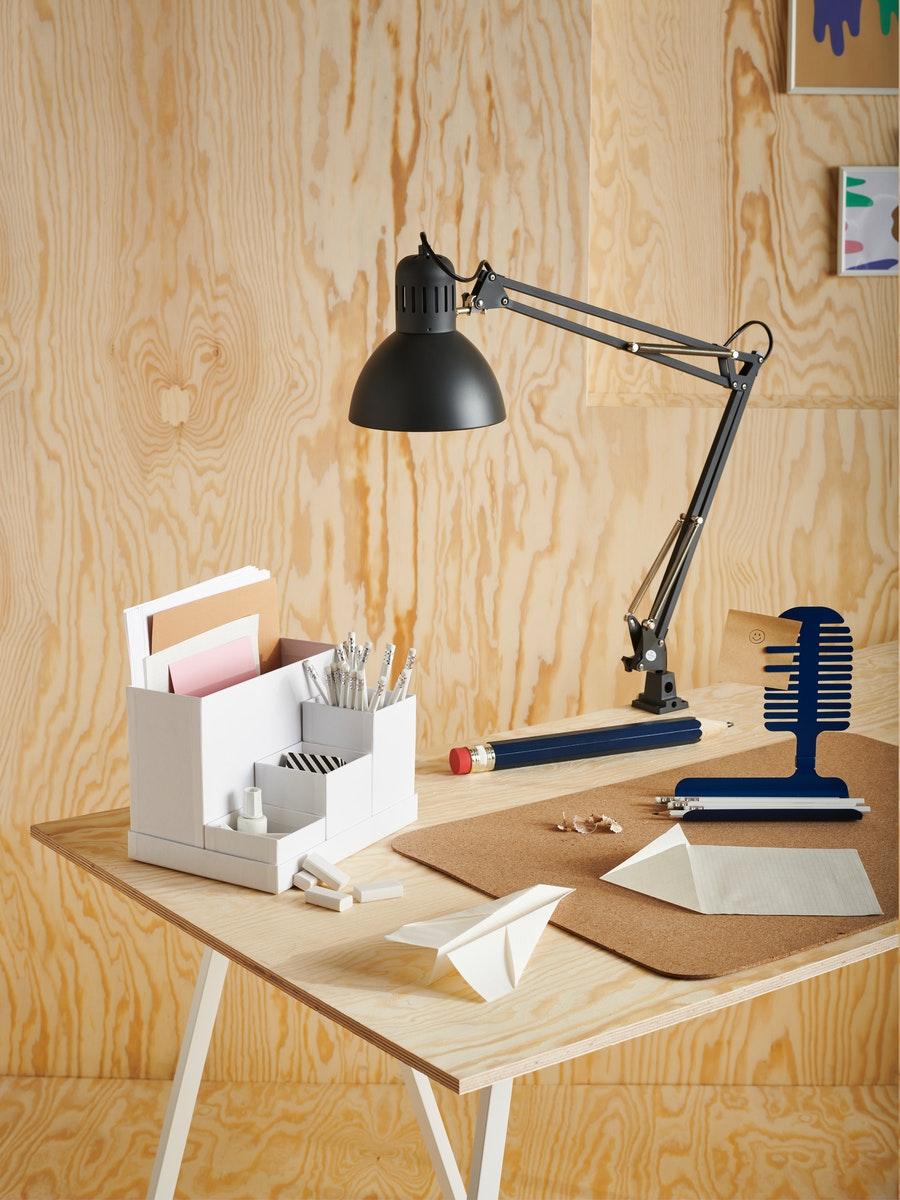 Una scrivania con un portaoggetti TJENA con cancelleria e sottomano SUSIG. La scrivania ha una lampada da morsetto nera TERTIAL.