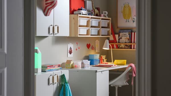 Una scrivania LÄRANDE bianca con un elemento contenitore estraibile, una sedia da scrivania per bambini bianca e un elemento contenitore da parete in pino/bianco.