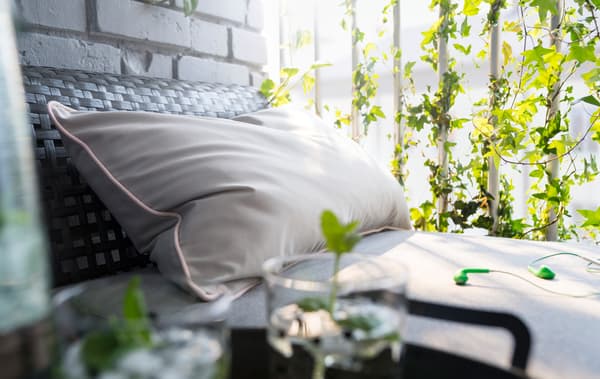 Una seduta modulare KUNGSHOLMEN crea un divano con cuscini su cui sono poste delle cuffiette verdi. In primo piano sono visibili due bicchieri e una bottiglia sopra un vassoio nero.