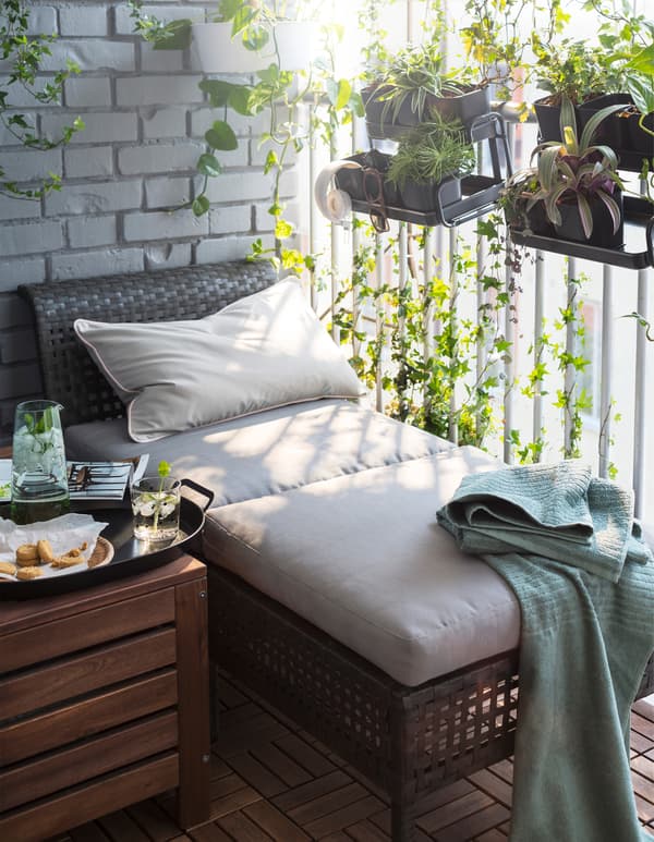 Una seduta modulare KUNGSHOLMEN realizzate in plastica effetto rattan e un tavolino con sopra un vassoio contente snack e bevande posti su un balcone.  Sulla ringhiera del balcone sono appese alcune piante tramite portavasi pensili BITTERGURKA