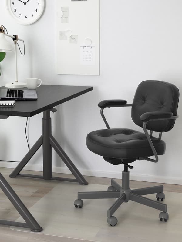 Una silla de oficina ALEFJÄLL negra forma un espacio de trabajo junto con un escritorio IDÅSEN en una habitación luminosa con paredes blancas.
