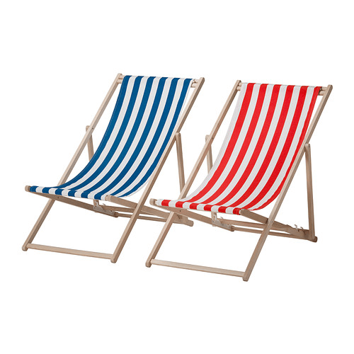 Una silla de playa de madera con un asiento de tela a rayas en azul y blanco junto a otra con un asiento a rayas en rojo y blanco.
