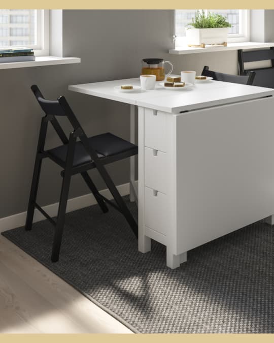 Una silla plegable negra en una mesa extensible blanca al costado de una ventana.