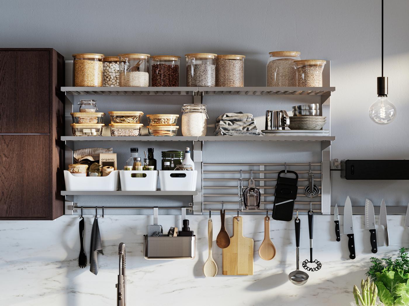 Una solución de almacenaje de pared KUNGSFORS en una pared con tarros de vidrio, cajas y varios utensilios de cocina junto a un armario marrón cerrado.