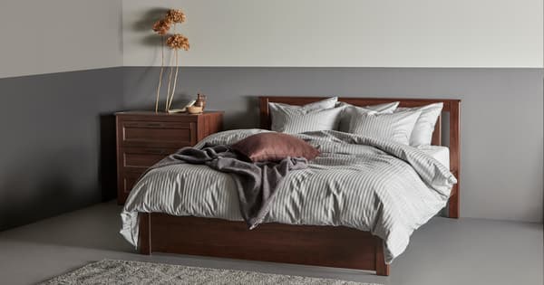 Una stanza con una struttura letto SONGESAND. Il letto ha coperte, cuscini e accanti un comodino. 