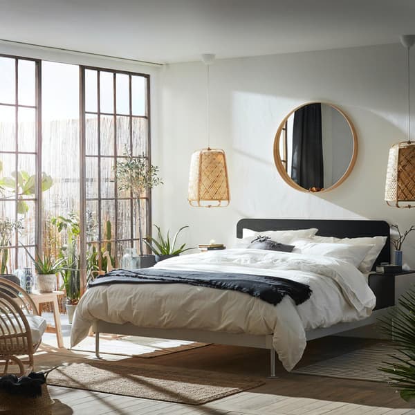Una stanza da letto con le finestre aperte che illuminano una struttura letto imbottita SLATTUM. Accanto al letto due lampade da parete e sopra uno specchio STOCKHOLM. 