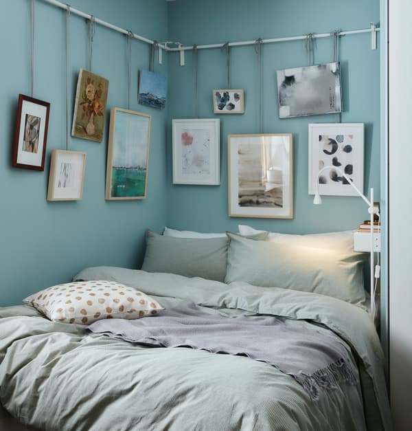 Una stanza da letto decorata con i toni dell'azzurro e con diversi quadri appesi con dei lacci a una sbarra che segue il percorso delle pareti.