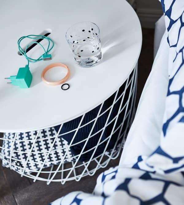 Una taula amb reixeta IKEA KVISTBRO blanca utilitzada com a emmagatzematge obert per guardar mantes i coixins.