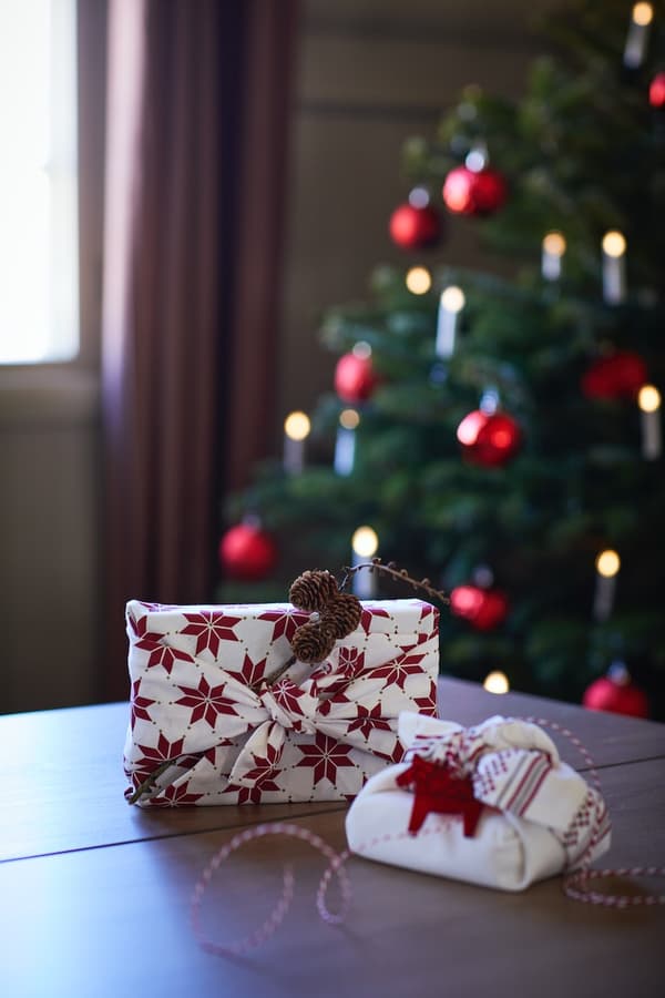 Una tavola con due pacchi di Natale realizzati con la tecnica del furoshiki. Sullo sfondo, si vede un alberio di Natale decorato.