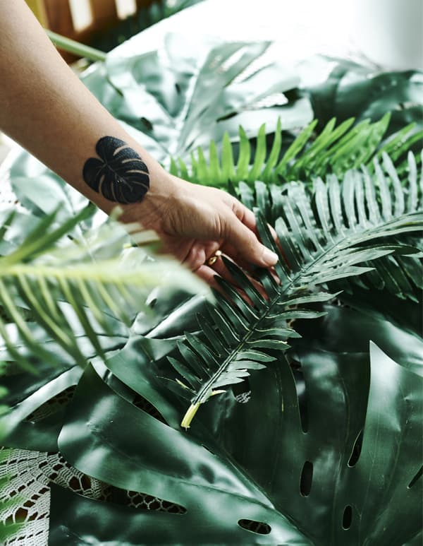 Una tavola decorata con grandi foglie e un braccio con il tatuaggio di una foglia - IKEA
