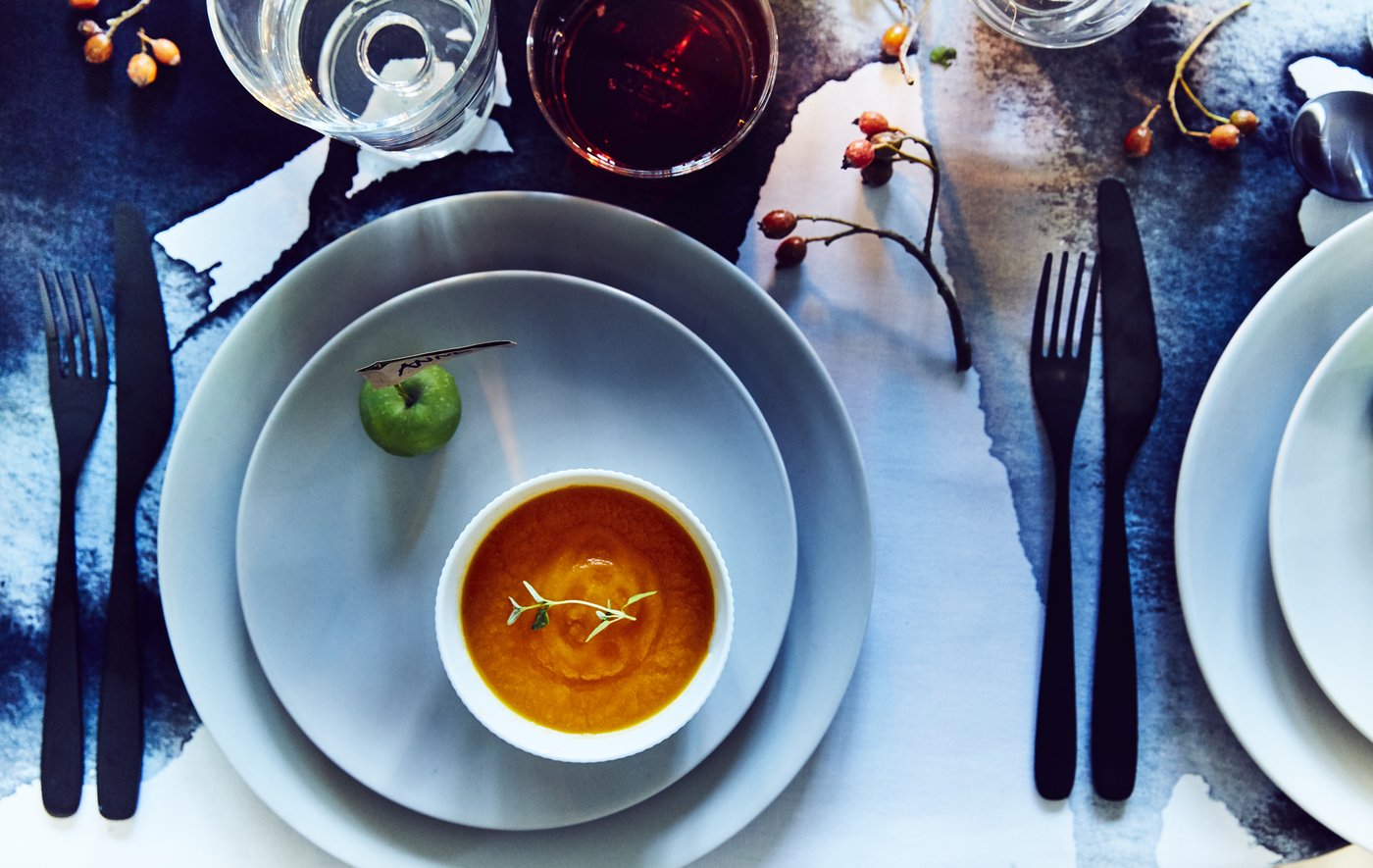 Una tavola pparecchiata con posate, ciotole e piatti. C'è un segnaposto personalizzato, una ciotola con una salsa o una zuppa.