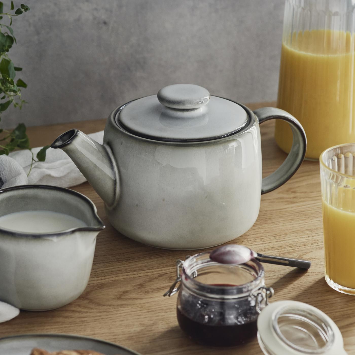 Una teiera grigia con una tazza accanto piena di latte