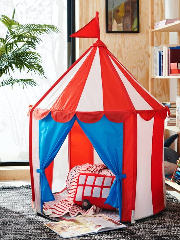 Una tenda CIRKUSTÄLT. All'interno, cuscini e coperta. Sul pavimento, un libro aperto.