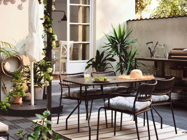 Una terrazza con un tavolo VIHOLMEN circondato da quattro sedie LÄCKÖ e una cucina all'aperto GRILLSKÄR con un barbecue a carbonella - IKEA.