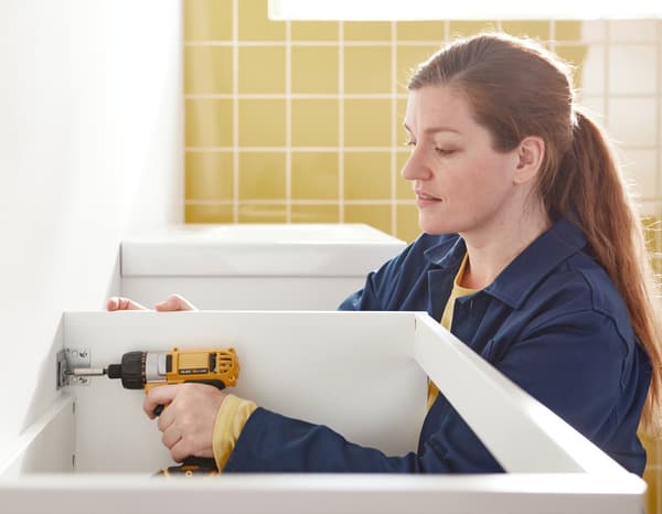 Una treballadora d'IKEA vestida de blau subjectant un tornavís elèctric i fixant una instal·lació al bany.