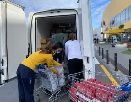 Una treballadora d’IKEA vestida de groc ajuda amb un carretó de la compra a carregar aliments en una furgoneta, amb el suport de dues persones més.