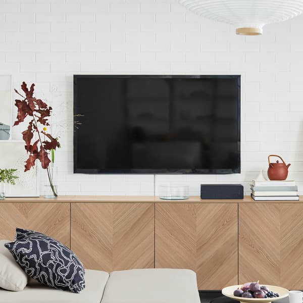 Una TV nera appesa a una parete bianca sopra un sistema componibile BESTÅ con frontali delle ante HEDEVIKEN in impiallacciatura di rovere - IKEA.