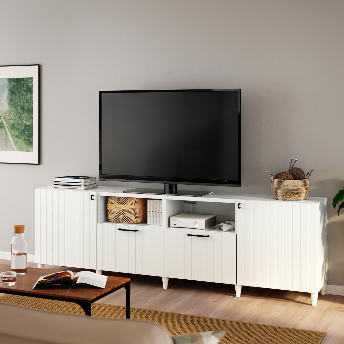 Una TV nera è posizionata su un mobile TV BESTÅ bianco con gambe KABBARP e ante/frontali SUTTERVIKEN bianchi.
