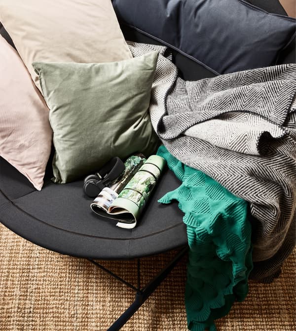 Una vista cenital de la mecedora IKEA PS 2017 en negro, con cojines y mantas.