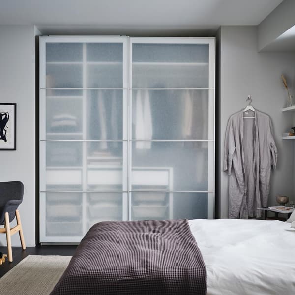 Una vista su una stanza da letto con in fondo un guardaroba con ante scorrevoli PAX / SVARTISDAL. Accanto al guardaroba è appeso un accappatoio rosa.  Sul letto è posato un plaid viola.
