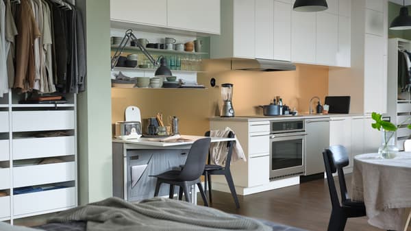 Una zona de cocina con alacenas SEKTION, sillas ODGER en color carbón, un lavavajillas ESSENTIELL y una mesa KALLHÄLL abatible.