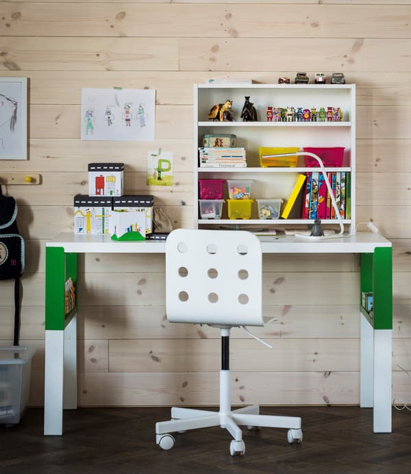 Una zona d'estudi infantil ben organitzada, amb un escriptori PÅHL en blanc i verd, una prestatgeria per a escriptori i caixes transparents amb tapa.