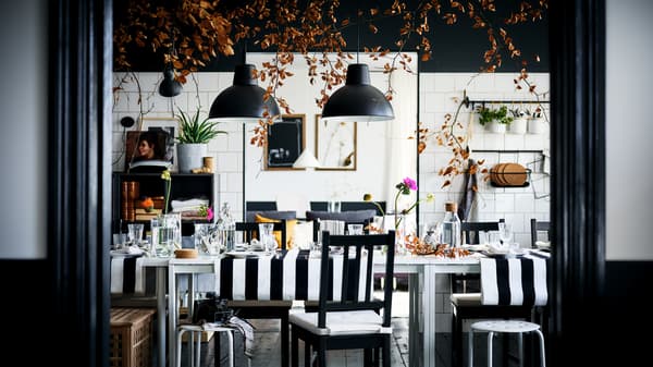 Una zona pranzo in bianco e nero con sedie STEFAN marrone-nero e sgabelli MARIUS, attorno a due tavoli MELLTORP bianchi.