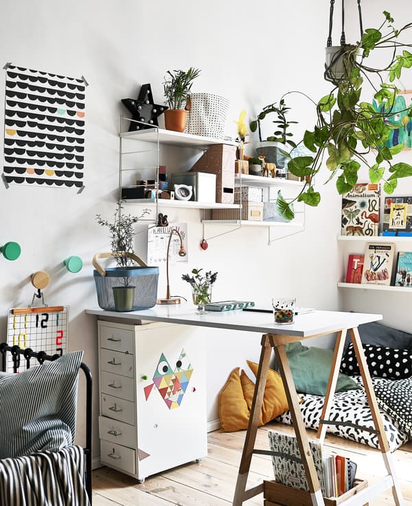 Una zona studio con piante a sospensione, mensole, una casettiera HEMNES, cuscini, un letto e oggetti artistici.