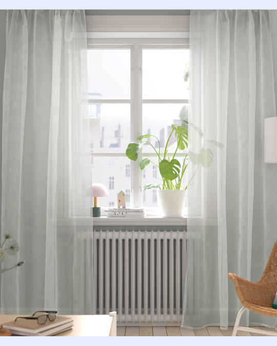 Unas cortinas de velo cubren una ventana de un living que tiene plantas en la corniza.